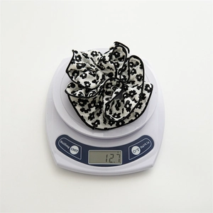 Close-up showing the floral fabric hair scrunchie weight at 12.7 grams on a white digital scale