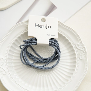 Detail of high-elasticity braided hair bands in dark grey on a white textured plate