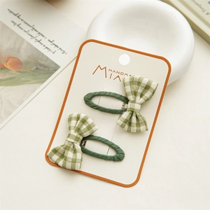 Detail of green plaid bow hair clips on a cream card, set against a soft aesthetic background