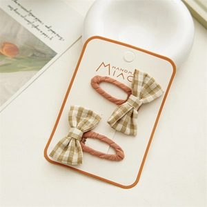 Detail of checkered bow hair clips in orange and beige fabric on white card