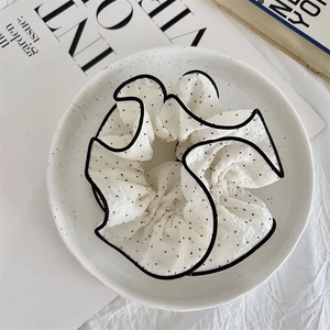 Close-up of a white polka dot scrunchie with black edging on a decorative porcelain plate