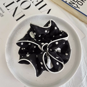 Detail of a large black polka dot chiffon scrunchie with white scalloped edge on a ceramic plate