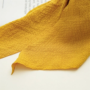 Detailed close-up of ginger yellow pleated fabric hair tie with distinctive crinkle texture