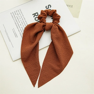 Detail of a brown plaid scrunchie with long ribbons on a minimalist magazine
