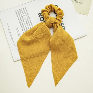 Detail of a ginger yellow plaid scrunchie with long ribbons on textured fabric
