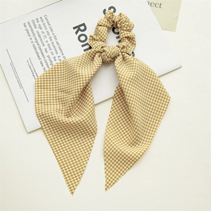 Macro view of yellow plaid scrunchie with long ribbons on minimalist magazine background