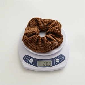 Detail showing solid brown knitted hair scrunchie weighing 28.3g on white scale