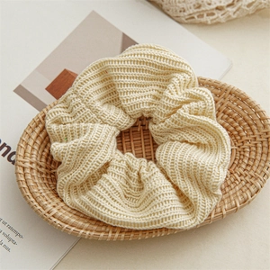 Macro shot of cream knit scrunchie with ribbed texture on a rustic rattan tray