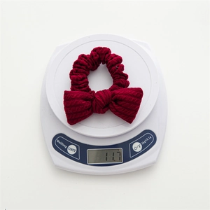 Red knit bow hair scrunchie with cable pattern showing 11.7g weight on a digital scale