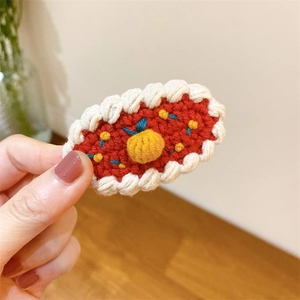 Détail d'une barrette crochetée rouge avec bords ondulés blancs et motif d'orange mignonne