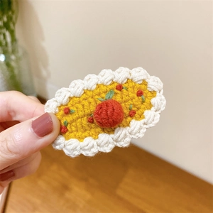 Vue détaillée d'une barrette cerise crochetée à la main avec laine jaune et dentelle blanche