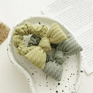 Close-up of ribbed knit bow scrunchies in green and yellow on a heart-shaped plate