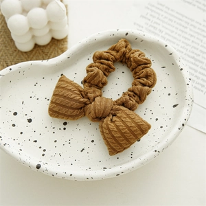 Detail of caramel brown knitted bow scrunchie with soft ribbed texture on ceramic tray
