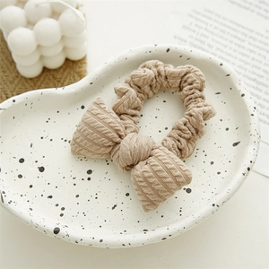 Chunky knit bow scrunchie in beige oat color on a minimalist ceramic tray