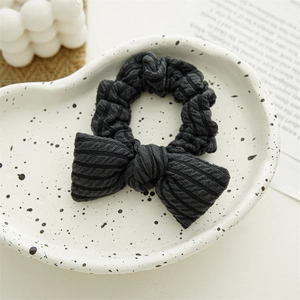 Detailed view of dark grey knitted bow scrunchie with soft ribbed texture on tray
