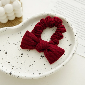 Detail of burgundy knitted bow hair scrunchie with waffle texture on ceramic plate