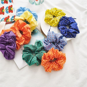 Detail view of a 9-piece set of polka dot and solid color fabric scrunchies on white linen