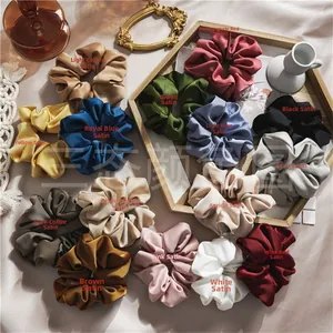 Flat lay of multiple satin scrunchies in 14 colors on a wooden tray with silk fabric