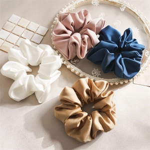 Detail showing oversized satin scrunchies in white, pink, navy, and camel with soft luster