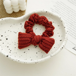 Detail of a dark red ribbed knit bow scrunchie on a decorative white artistic plate
