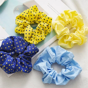 Set of four pastel and polka dot scrunchies in yellow and blue on a textured surface