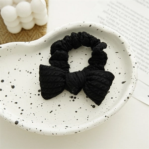Close-up of a black knitted bow scrunchie with textured fabric on a ceramic tray
