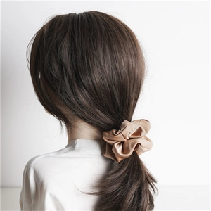 Detail view of champagne gold satin scrunchie styled in a low ponytail on a model