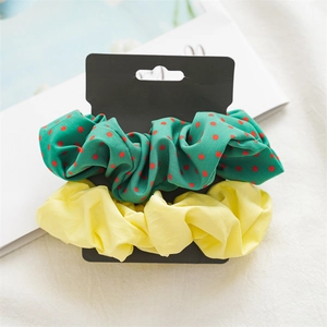 Close-up of green polka dot and solid yellow scrunchies set on a black display card