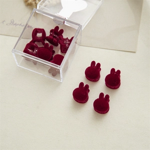 Detailed view of red velvet bunny hair clips in a clear box on beige paper background