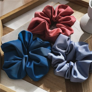 Detailed view of three thick satin scrunchies in navy blue, brick red, and lilac on a tray