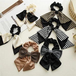 Detail view of houndstooth and solid color bow hair scrunchies on a minimalist background