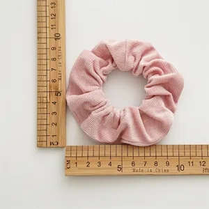 Chouchou en velours rose mesuré sur fond blanc avec une règle en bois graduée