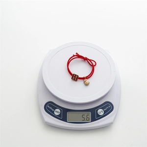 Détail d'un bracelet rouge porte-bonheur avec pendentifs dorés pesé sur une balance digitale