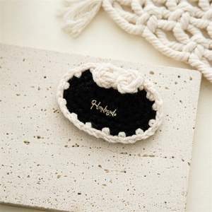 Detail of a handmade black knitted hair clip featuring a cream bow and gold metal tag