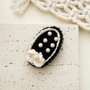 Detailed close-up of handmade black wool hair clip with elegant white pearls and knit flower