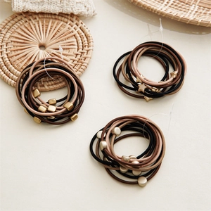 Close-up of earth-toned elastic hair ties with matte gold geometric charms on a soft base