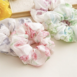 Close-up of floral satin scrunchies with pink roses and purple flowers on a white tray