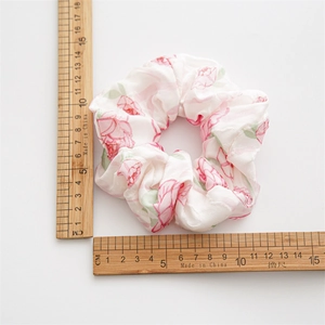 Floral satin scrunchie with pink rose patterns measured by rulers on a white background