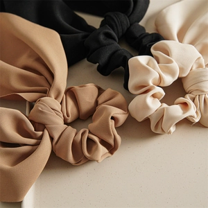 Macro view of textured ribbon scrunchies in black, brown, and cream with bow streamers