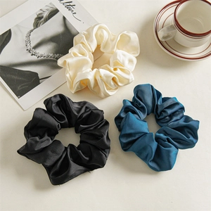 Three elegant satin scrunchies in cream, black, and blue colors on a minimal desk