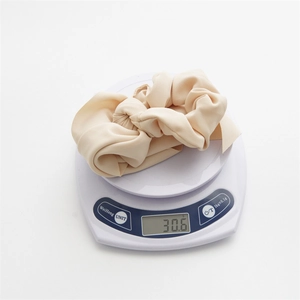 Close-up showing a beige textured fabric hair scrunchie weighing 30.6g on a digital scale