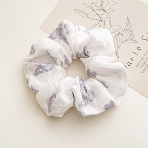 Detailed close-up of white satin scrunchie with delicate purple butterfly patterns