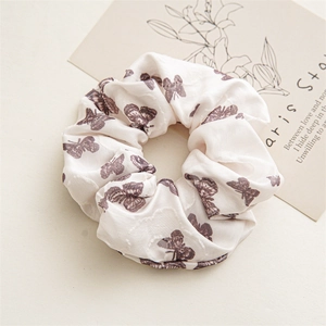 Detailed view of cream floral satin scrunchie with brown butterfly print and soft pleats