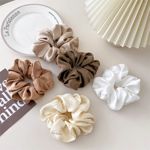 Detailaufnahme von fünf Satin-Haargummis in Erdtönen auf einem eleganten Porzellanteller