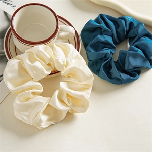 Elegant satin scrunchies in cream and teal blue on a decorative ceramic saucer