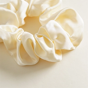 Detailed close-up of elegant beige satin scrunchie showing glossy texture and pleats