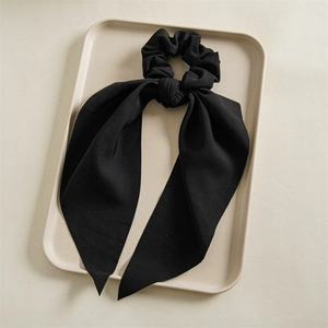 Detail of elegant black pleated scrunchie with long ribbons and twill fabric texture