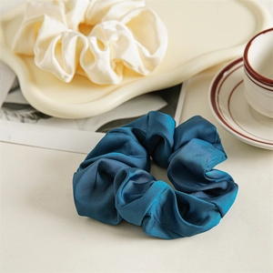 Close-up of elegant satin scrunchies in cream and peacock blue on a ceramic tray
