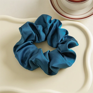 Detail view of a luxury navy blue satin scrunchie on a stylish decorative tray