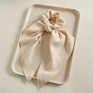 Detail of light beige bow hair scrunchie with long ribbons on a textured tray